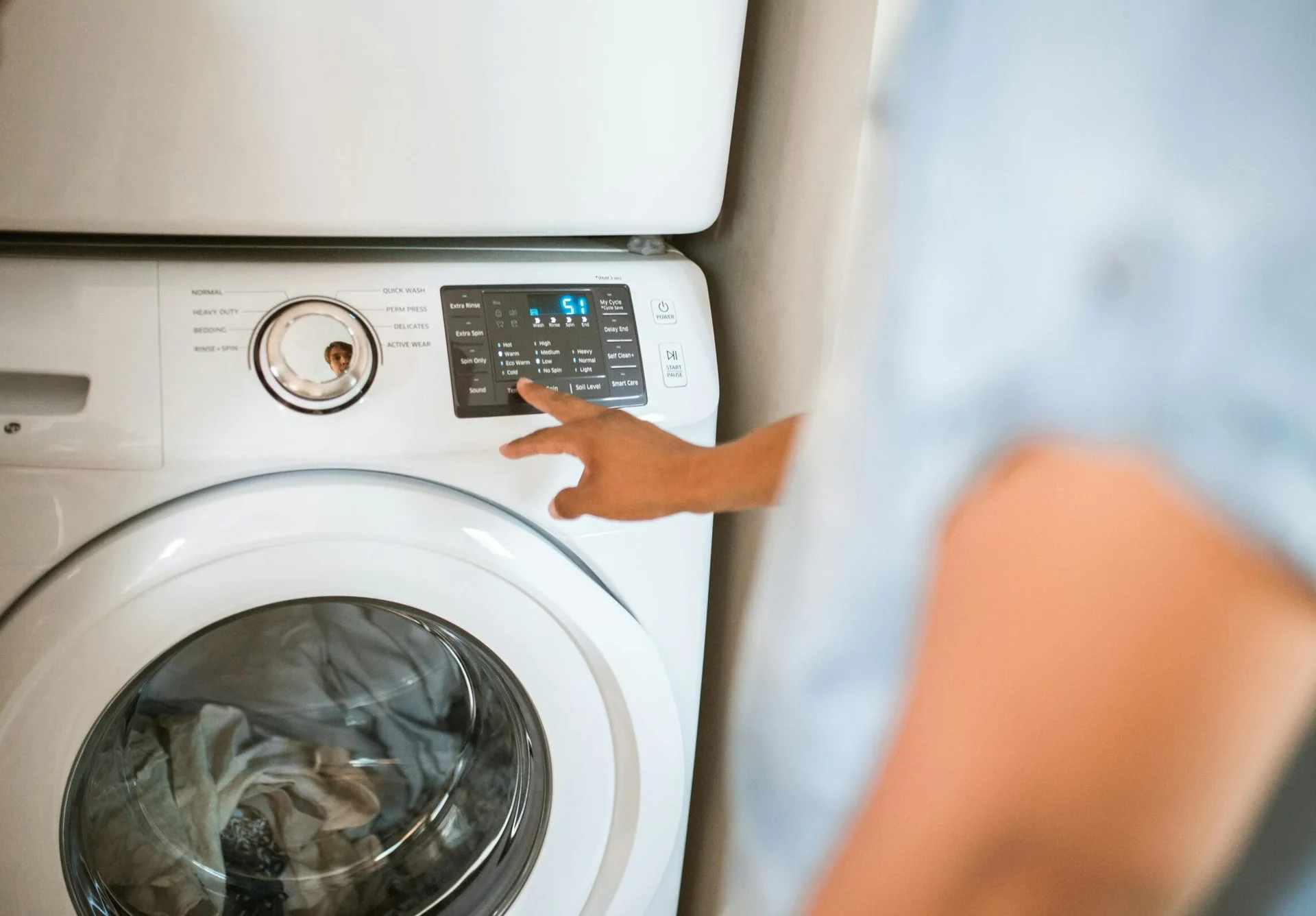 Hand selecting laundry options on a digital washing machine control panel indoors.
